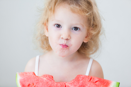 cute little baby girl eating watermelon slice on light backgroundの写真素材