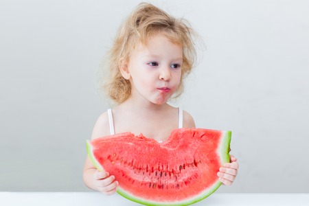 cute little baby girl eating watermelon slice on light backgroundの写真素材