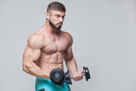 Muscular bodybuilder guy doing exercises with dumbbell over grey backgroundの写真素材