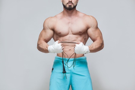 Sport, activity. Muscular Fighter kickbox with skipping rope. Muscular men grey background.の写真素材