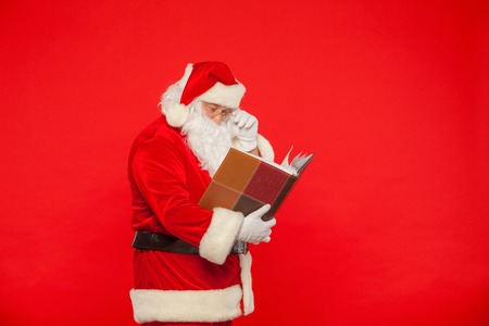Santa Claus reads old book, on a red background. Christmasの写真素材