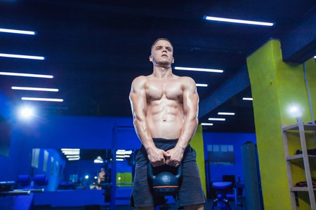 Portrait of a young muscular man lifting kettlebell in gym