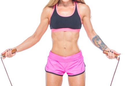 Attractive, sexy, muscular girl in pink shorts and a black top jumps over a modern rope with wooden handles. Cardio-training. Fitness, healthy lifestyle concept. Isolated on the white background.の写真素材