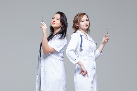 Two female doctors standing back-to-back hold ready-to-inject syringesの写真素材