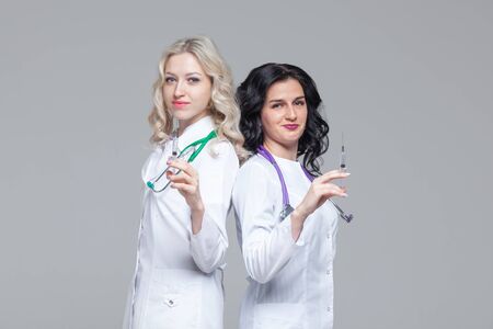 Two female doctors standing back-to-back hold ready-to-inject syringesの写真素材