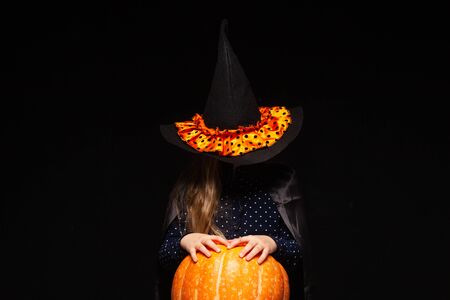 Halloween Witch with Pumpkin on black background. Beautiful young surprised woman in witches hat and costume holding pumpkin. Wide Halloween party art design. Copy-paste. Witch craft concept. Spider on hat.の写真素材
