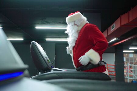 Santa Claus training at the gym on Christmas Day. Santa Claus running in machine treadmill at fitness gym club.の写真素材