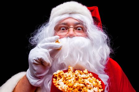 Christmas. Photo of Santa Claus gloved hand With a red bucket with popcorn, on a black backgroundの写真素材