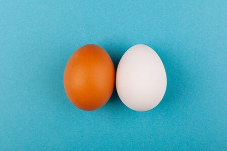 Two chicken eggs white and brown on a blue background. The concept of a healthy lifestyle, getting...