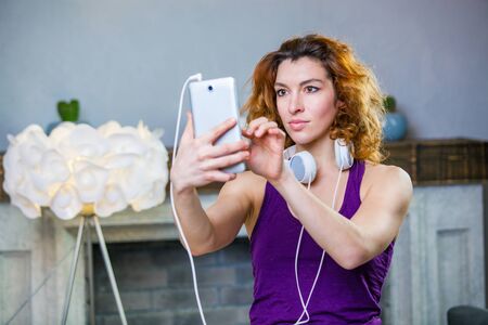Portrait of an attractive woman with headphones on and holding smartphone in her hands choosing musicの写真素材