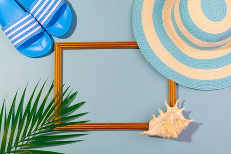 Top view on striped blue hat, flip-flops, palm leaf, seashell and frame for vacation photos on...