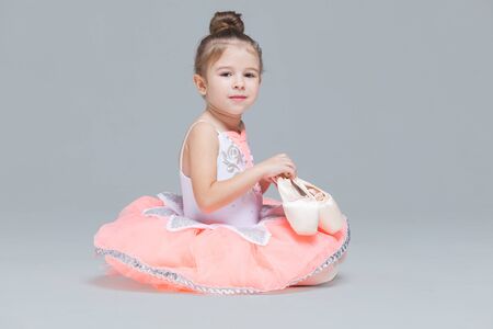 Cute adorable ballerina little girl in pink tutu sitting on the floor holding ballet shoesの写真素材
