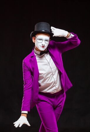 Portrait of male mime artist, isolated on black background. Man in a purple suit is happily posing for the cameraの写真素材