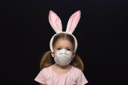 Concept of coronavirus and air pollution. A little girl wears a mask for protection and an Easter Bunny ears costume.の写真素材