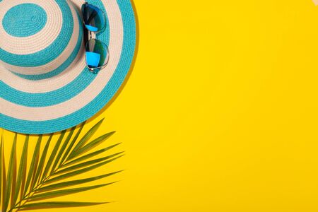 Top view on beach accessories on yellow background - sunglasses, striped blue hat and palm leaf. Concept of beach holiday, sea tour, warm sunny summer. Advertising spaceの写真素材