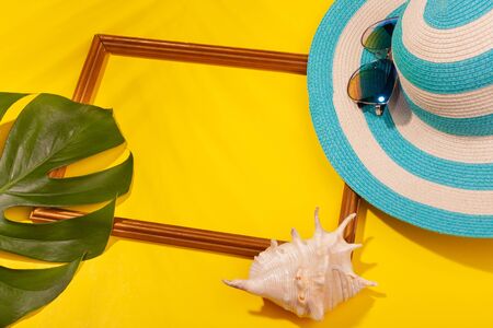 Top view on striped blue hat, sunglasses, monstera leaf, seashell and frame for vacation photos on yellow background. Concept of beach holiday, sea tour, warm sunny summer. Copy-paste.の写真素材