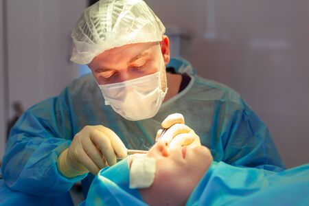 Close up of the face of a patient who is undergoing blepharoplasty. The surgeon cuts the eyelid and...