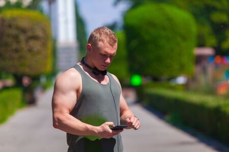 Muscular sporty man with headphones on the neck is choosing music on the player for a run in the summer Parkの写真素材