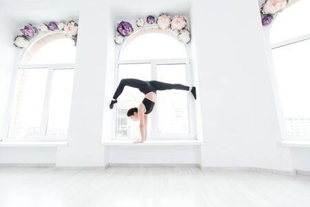 Young woman practicing yoga, standing in handstand exercise on the windowsill, working out wearing black sportswearの写真素材