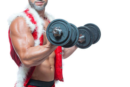 Sexy Santa Claus. Bodybuilder young handsome santa clause smile holds a dumbbells and shows off abs cubes at New Years eve and Christmas winter holiday white background.の写真素材