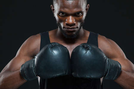 Front view shot of young African American boxer wearing gloves is posing isolated on a dark backgroundの写真素材