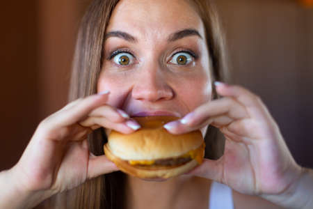 Close up of beautiful hungry young brunette is about to bite a delicious hamburger. Concept of junk food and fast foodの写真素材
