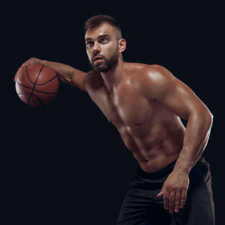 Portrait of a very muscular naked man playing basketball isolated on black backgroundの写真素材