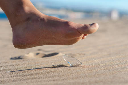 Woman going on the beach and risking of stepping on a splinter of broken bottle glass, which is lying on the littered sandの写真素材