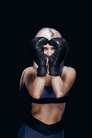 A sporty blonde in boxing gloves holds her hands in front of her face smiles and prepares for...