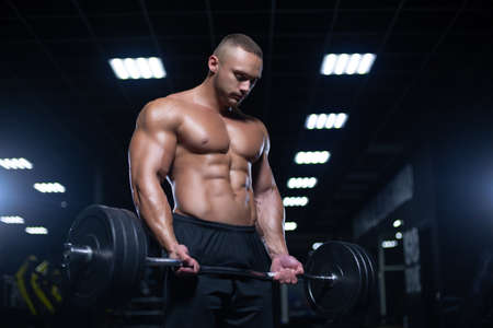 Muscular sexy bodybuilder is working out doing weight lifting of the barbell in gymの写真素材