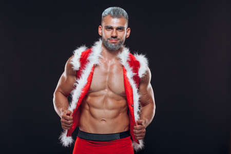 Sexy Santa Claus . Young muscular man wearing Santa Claus hat demonstrate his muscles. Isolated on black background.の写真素材