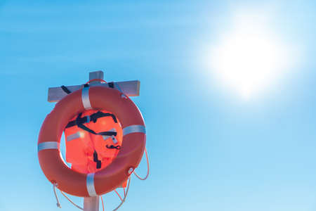 Bright lifebuoy and life jacket on the beach against the blue skyの写真素材