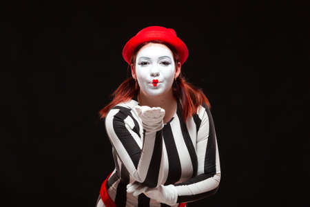 Portrait of female mime artist performing, isolated on black background. Woman blows a kiss posing in striped dressの写真素材