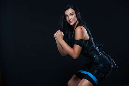 A young athletic woman in an EMS suit exercising on an isolated black background. EMS training. Electro muscular stimulation machine.の写真素材
