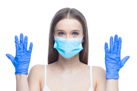 Studio shot on white background of a beautiful young woman wearing mask and latex gloves protected from coronavirus standing with raised hands stressed by quarantineの写真素材