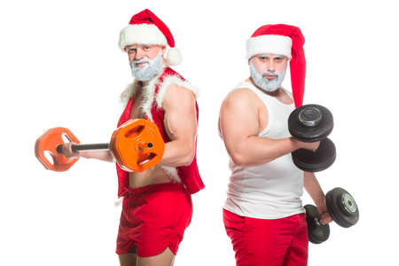 Christmas. Portrait of two strong muscular bearded athletes in Santa Claus costumes, training by lifting barbells isolated on white backgroundの写真素材