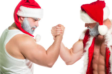 Christmas. Close up portrait of two serious confident muscular Santa Clauses performing techniques from arm wrestling isolated on white backgroundの写真素材