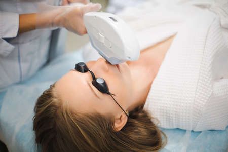 Close up of a young woman face while cosmetologist does the procedure for laser hair removal of unwanted hair of the face and upper lip in a beauty salonの写真素材