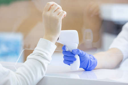 Close up of a female hand being measured body temperature with a contactless thermometer by the...