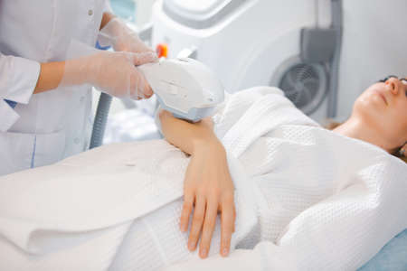 Close up laser hair removal on the arm of a young girl by a professional specialist in a modern cosmetology officeの写真素材
