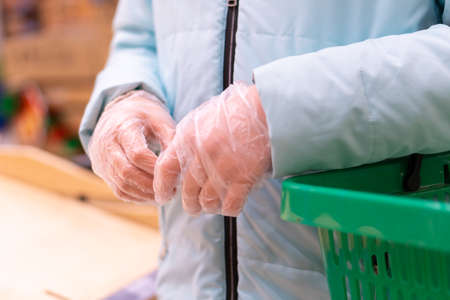 Close up of woman hands in gloves holding a shopping basket. Shopping during quarantine in compliance with the rules to prevent the spread of coronavirus infection in a pandemicの写真素材