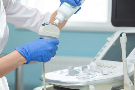 Closeup of the application of medical gel on the ultrasound diagnostic sensor. The doctor is...
