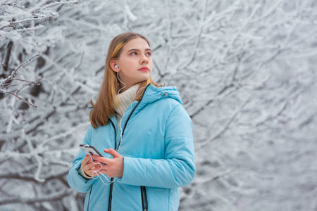 Front view of a beautiful teenage girl listening to music with headphones in a smartphone while...