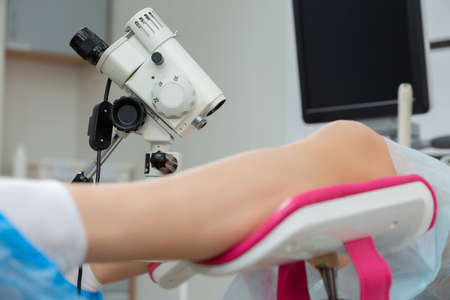 A gynecologist performs a colposcopy on a young girl in a gynecological chair in a modern medical...