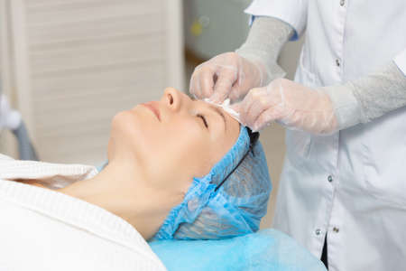 Photo of professional female cosmetologist using sponges to wash the face of a woman client preparing for a cosmetic procedure. Rejuvenating and moisturizing proceduresの写真素材
