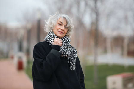 Portrait of a beautiful mature woman walking in autumn park in a coat and warm trendy scarfの写真素材