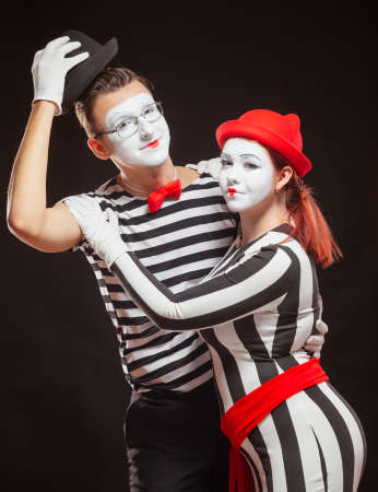 Portrait of two mime artists performing, isolated on black background. Man raised his hat and woman nestled against him. Symbol of greeting, introduction, friendshipの写真素材