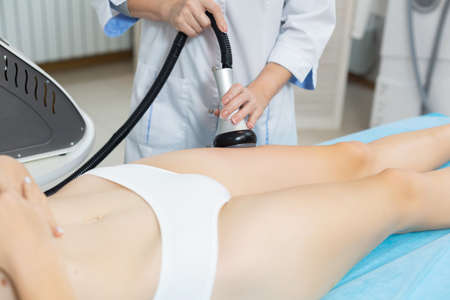 Slender woman receives a cavitation procedure getting anti-cellulite and anti-fat therapy on her tight buttocks in a beauty salon for splitting fat cells under the influence of ultrasound from a professional cosmetologist.の写真素材