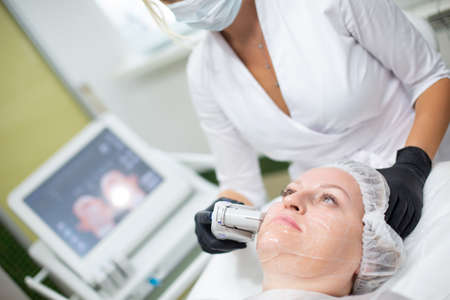 A woman in a cosmetology office receives a SMAS lifting procedure. Non-surgical ultrasound facelift, rejuvenation, moisturizing, getting rid of wrinkles, skin tone and elasticityの写真素材
