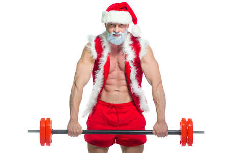 Christmas. Strong muscular Santa Claus with grey beard wearing christmas hat and red shorts is lifting a heavy barbell in a gym performing a workout isolated on white background.の写真素材
